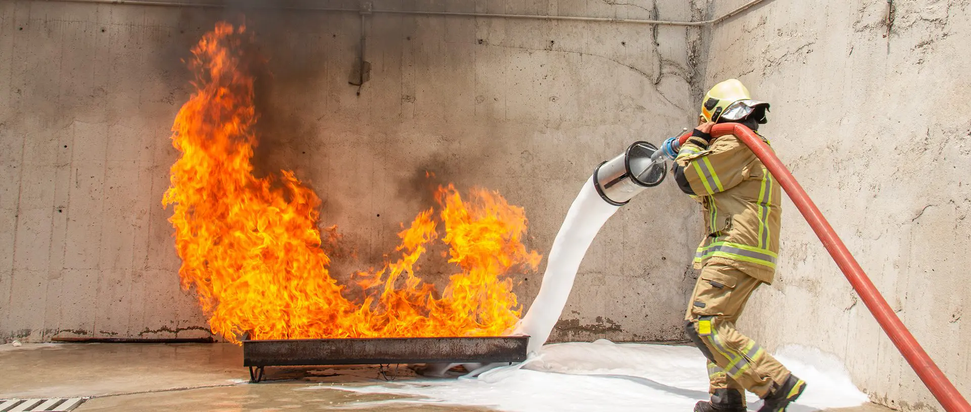 Firefighter extinguishing blaze with foam hose.
