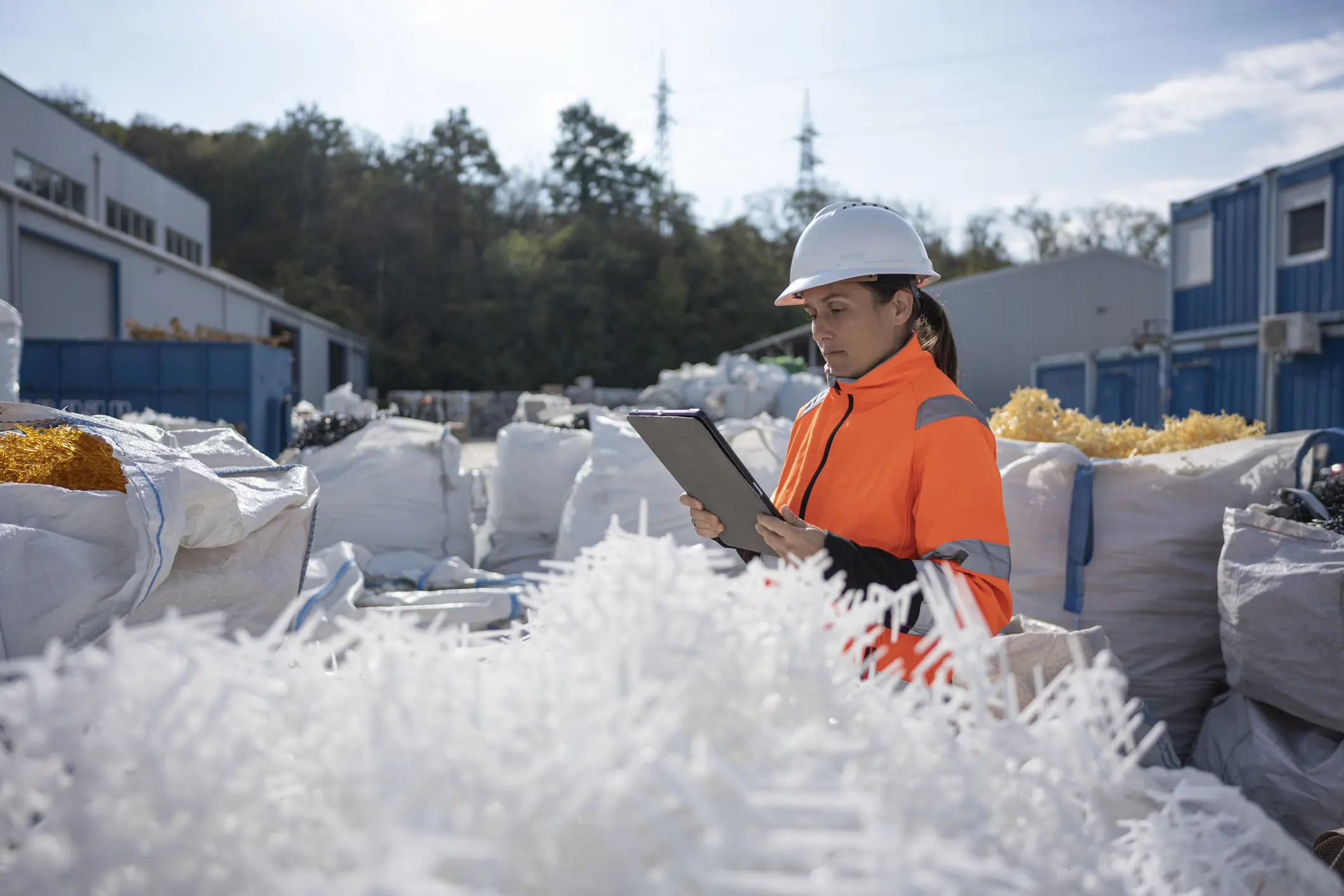 Female worker at industrial recycling site, wearing safety gear &amp; hardhat, inspects sorted plastic pellets for reuse in manufacturing. Circular economy concept.